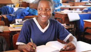 A girl is smiling while writing in her notebook.