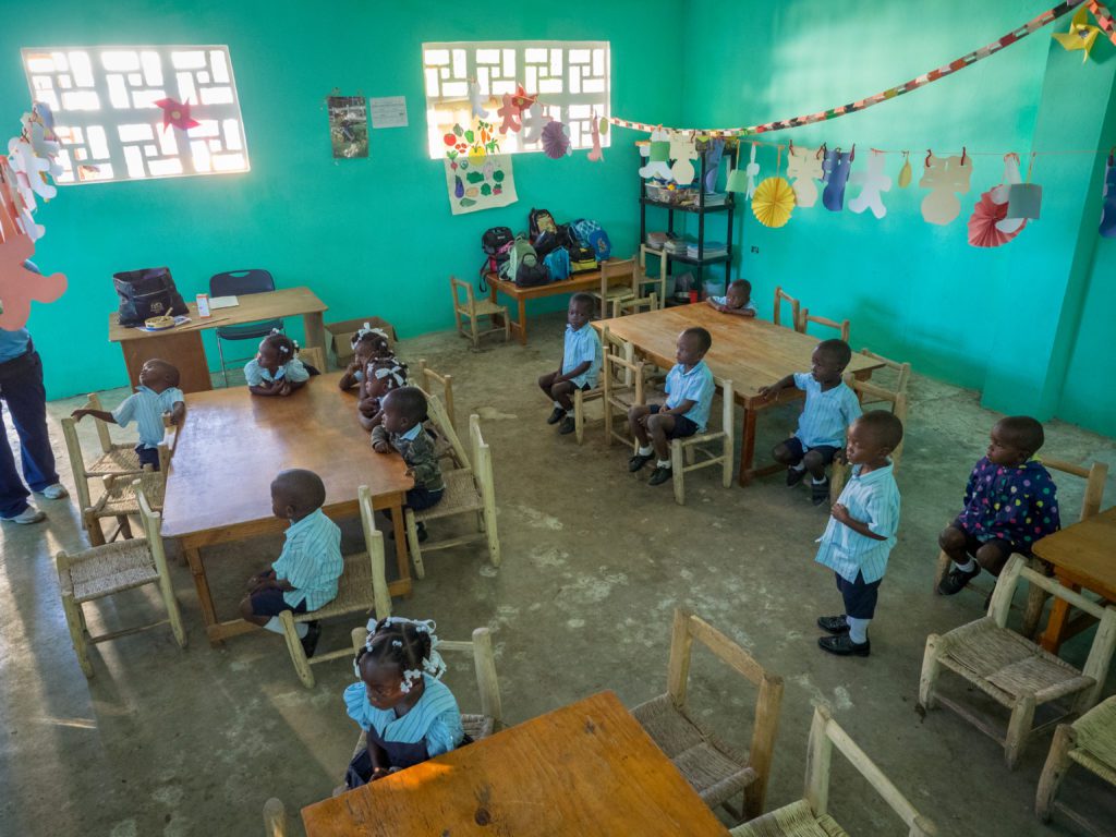 A group of children sitting at tables in a classroom.