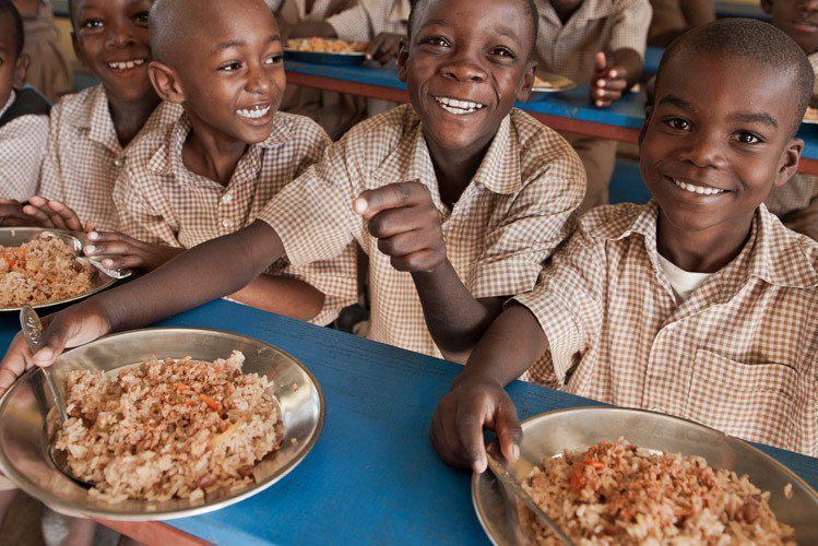 A group of young boys sitting at a table eating food.