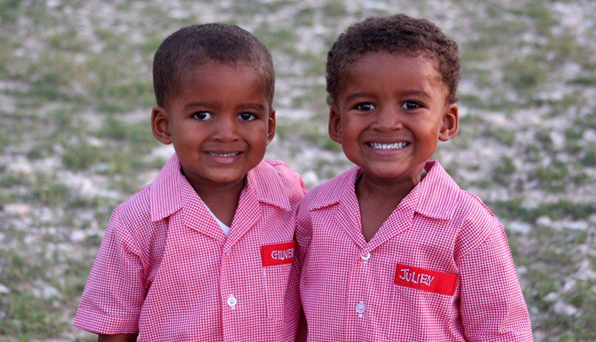 Two young boys in pink shirts smiling for the camera.
