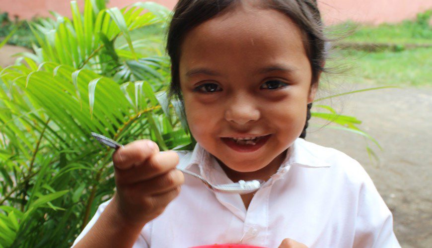 A little girl holding a spoon and smiling.